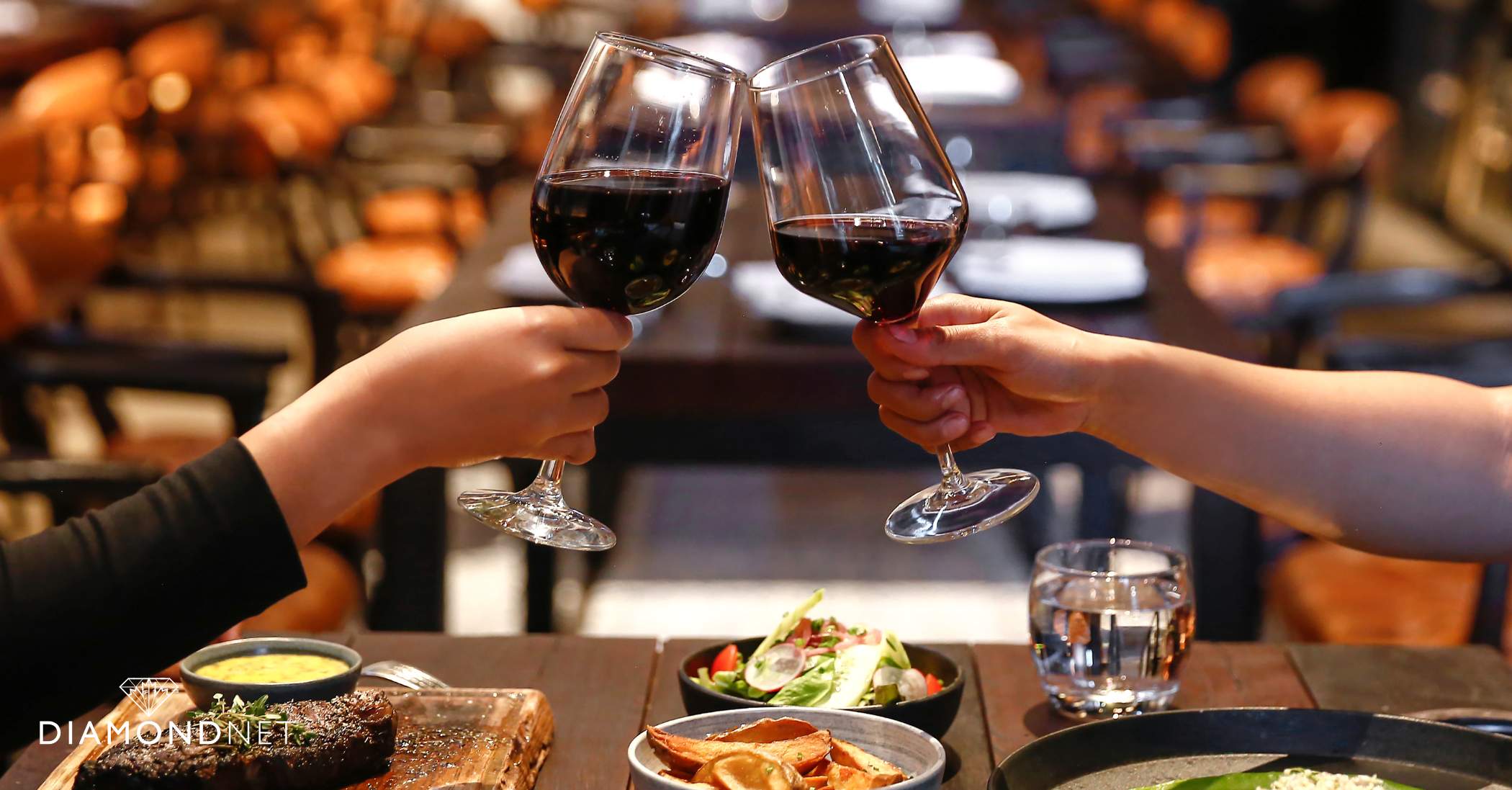 Two people raise their wine glasses in a toast, celebrating a special romantic anniversary occasion.