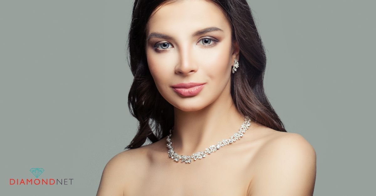 A bride in a wedding dress assists another woman with a matching diamond necklace, enhancing her bridal look
