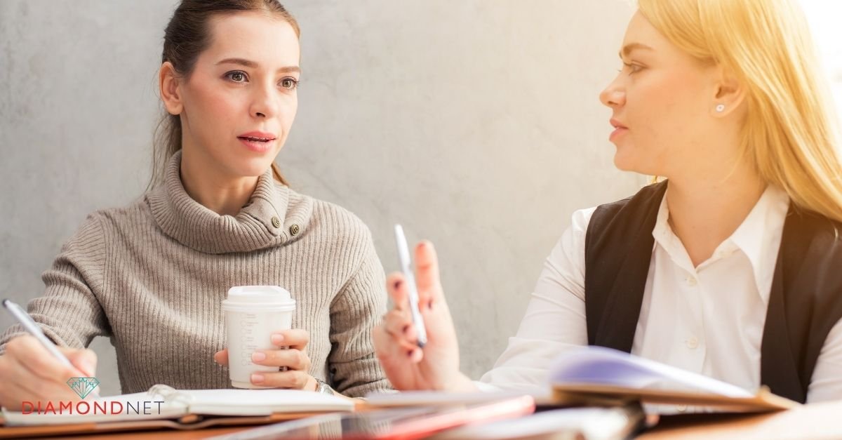 Two women collaborating at a desk, reviewing a wedding planning guide together